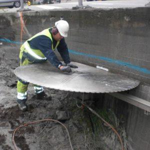 En arbeidstaker bruker en stor sirkelsag for å kutte betong ved en byggeplass.