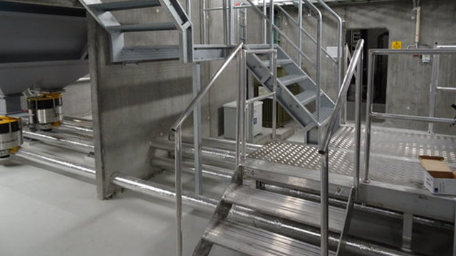 Trappegang med metalltrapper og plattformer i en industriell bygning med grå betongvegger.