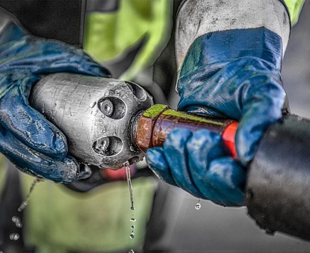 En person med blå hansker holder en metallrørdel som drypper vann.