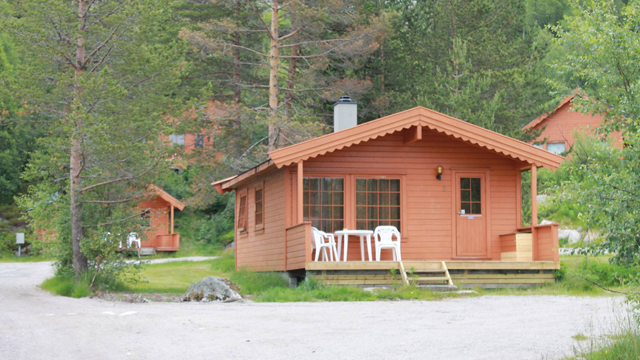 Koselig hytte i skogen med trestoler på terrassen og omgivende trær.