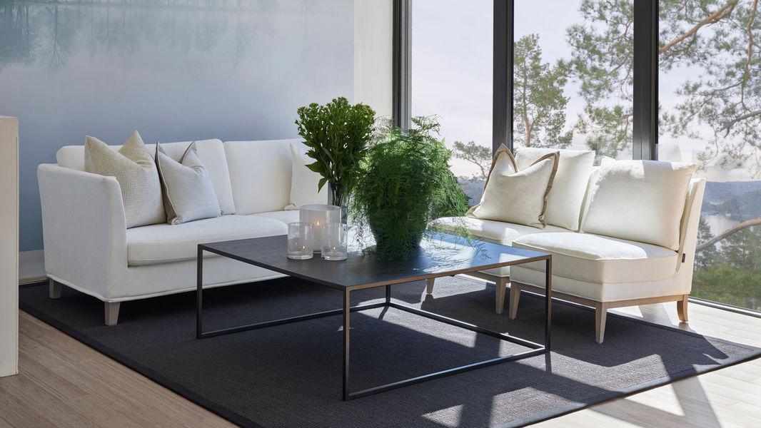 Moderne stue med hvite sofaer, et svart bord og grønne planter i et lyst rom med store vinduer.