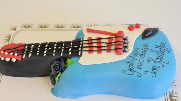 En kake formet som en gitar med blå og svart glasur, dekorert med roser og tekst.