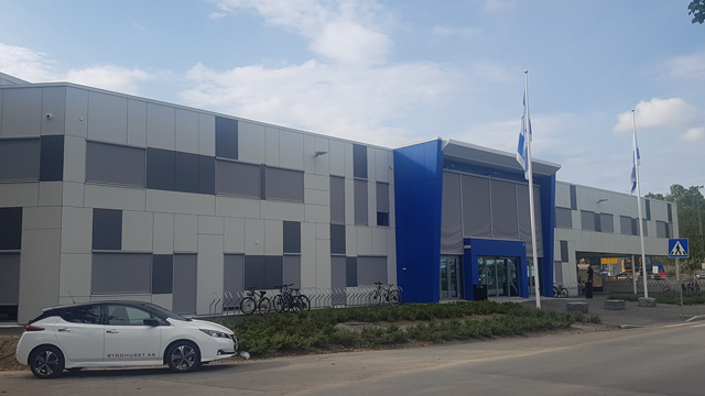 Moderne kontorbygg med blå detaljer, sykler parkert foran og en elbil ved siden av.