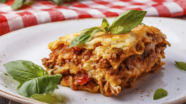 Lettvint lasagne med kjøttdeig, tomatsaus og basilikum på en hvit tallerken med rød- og hvitstripete duk.