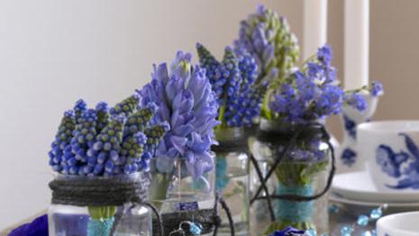 Blå blomster i glasskrukker på et bord, dekorert med blå detaljer og servise.