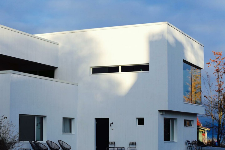 Moderne hvitt hus med store vinduer og en klar blå himmel i bakgrunnen.
