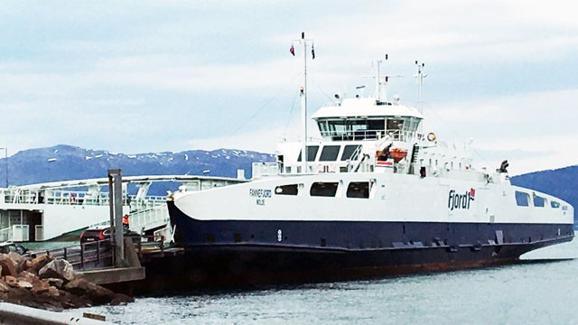 Ferge ved kaien med fjell i bakgrunnen, klar til avgang fra havnen.