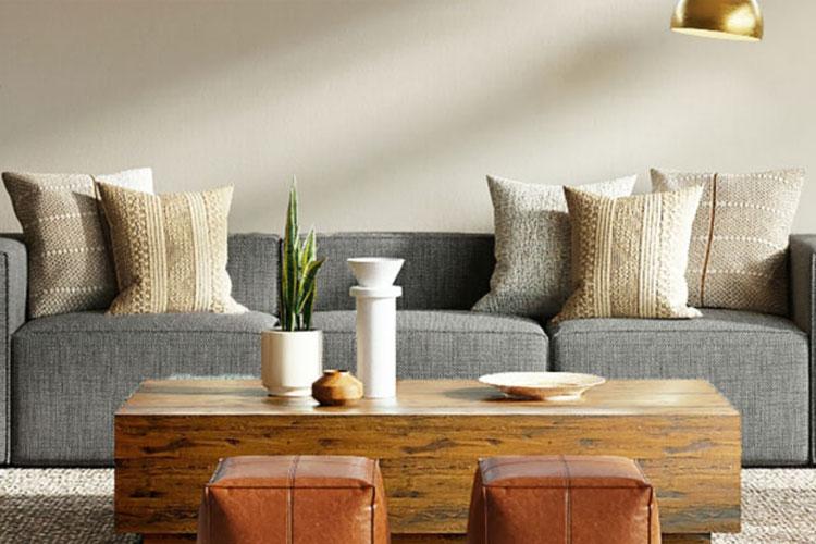 Moderne stue med grå sofa, dekorative puter, et trebord og to skinnpuffer. Grønne planter gir liv til rommet.