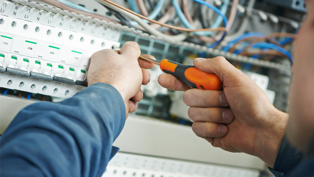 En elektriker bruker en skrutrekker for å jobbe med elektriske ledninger i et sikringsskap.