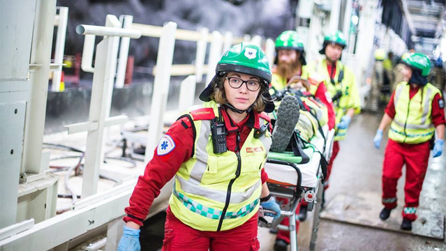 En gruppe redningsarbeidere i røde uniformer og hjelmer jobber i en røykfylt situasjon.