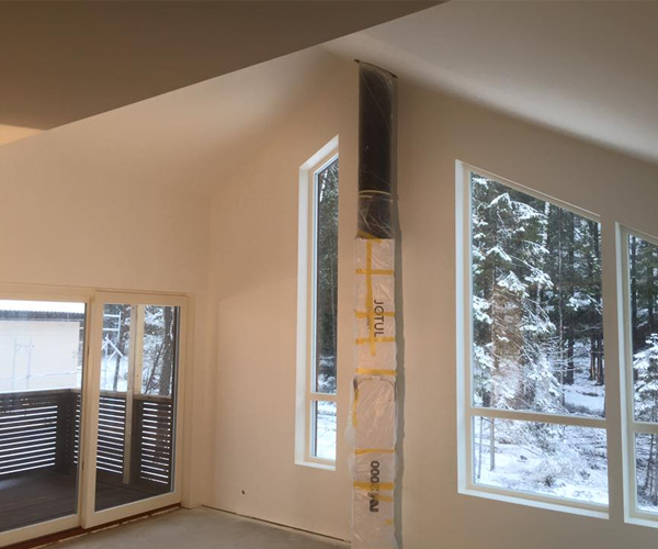 Moderne stue med store vinduer, snødekt landskap utenfor og en ventilasjonskanal i hjørnet.