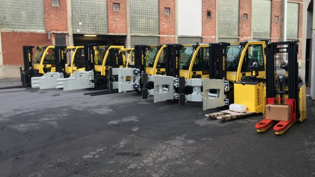 Flere gule gaffeltrucker parkert i en rekke på en asfaltbelagt gårdsplass.