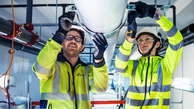 To personer i verneutstyr jobber sammen med rørinstallasjon i en moderne bygning.