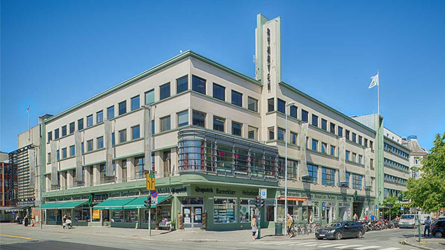 Moderne bygning med flere etasjer, store vinduer og butikker i første etasje, beliggende i en bygate.