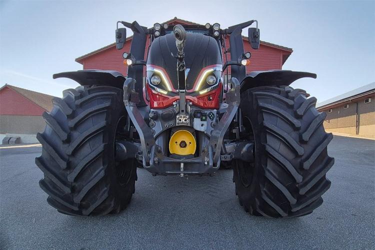 En stor traktor med kraftige dekk og unike frontlykter, stående på en gårdsplass med bygninger i bakgrunnen.