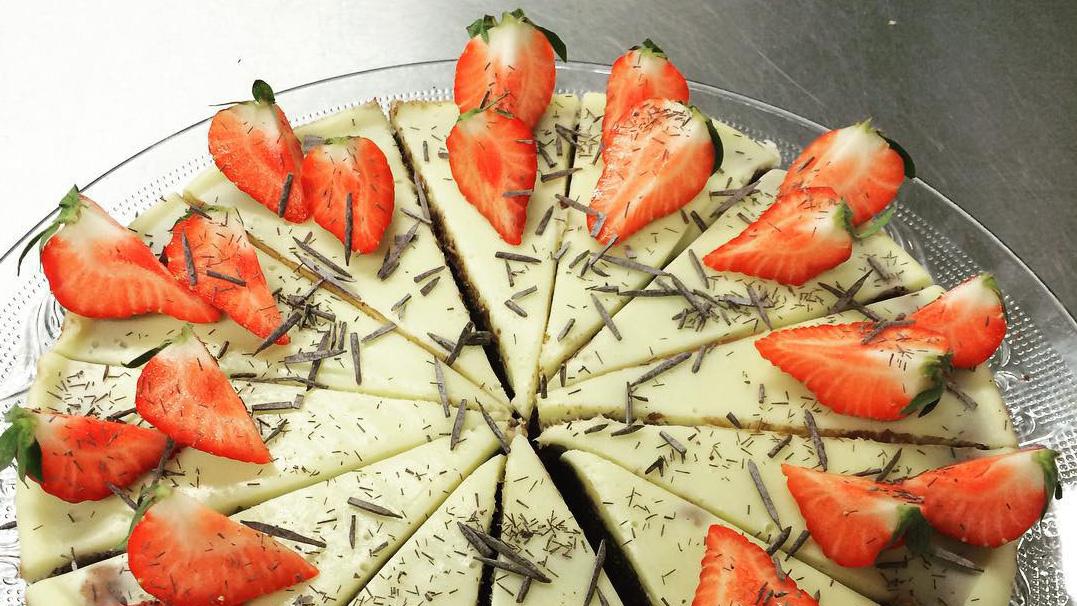 En kake med hvit sjokolade, pyntet med friske jordbær og sjokoladeflak, delt i stykker på en glassfat.
