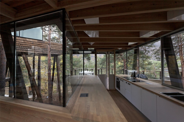 Moderne kjøkken med glassvegger og treverk, omgitt av natur i et stilrent hus.