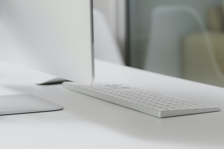 Moderne datamaskin med et stilrent tastatur på et lyst skrivebord i et kontormiljø.