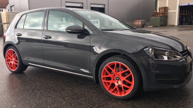En grå Volkswagen Golf med oransje felger parkert på en asfaltvei.