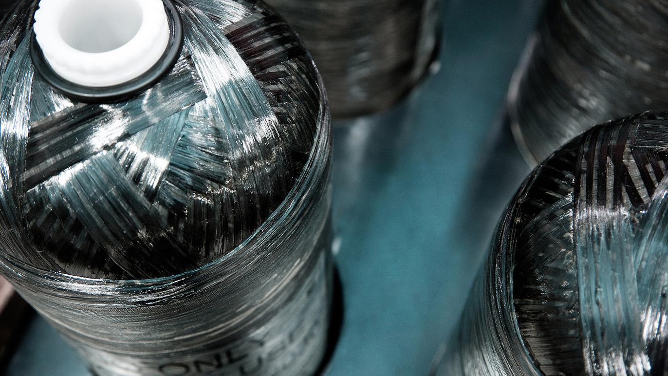 Flasker med metalltråd, stablet på en blå overflate, med fokus på teksturen og refleksjonen av lyset.
