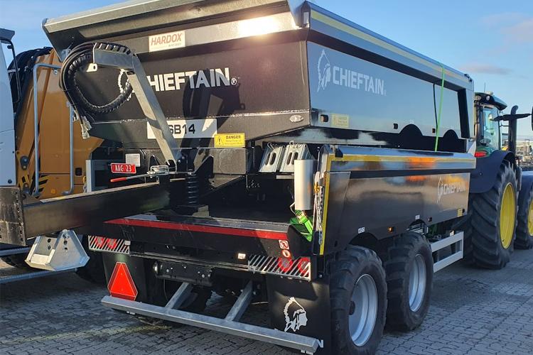 En Chieftain tilhenger med åpen bakluke, parkert ved en traktor på en byggeplass.