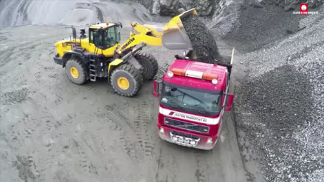 En stor hjullaster tømmer grus i en lastebil på en steinbrudd.