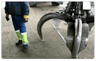 En arbeidstaker står ved siden av en stor metallklo som brukes til løfting i en industriell setting.