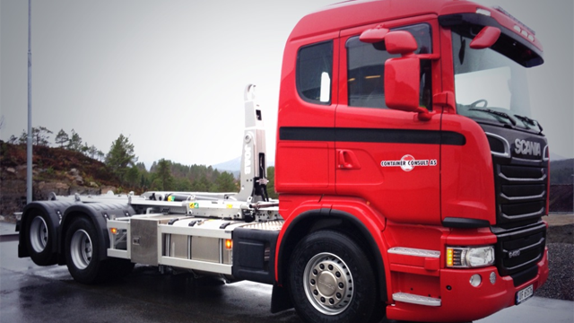 Rød Scania lastebil med moderne design, stående på en vei med natur i bakgrunnen.