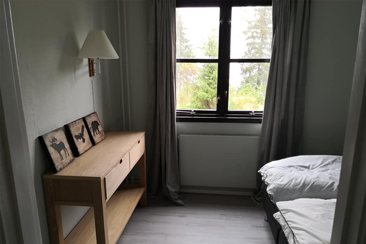 Lyst rom med en seng, en kommode i tre og vindu med gardiner som gir utsikt til naturen.