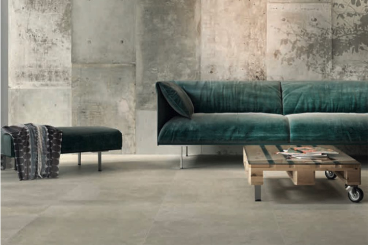Moderne stue med grønn sofa, trebord på hjul og betongvegg, som gir et stilrent og industrielt preg.