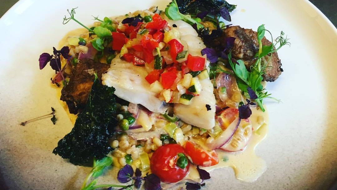 En tallerken med stekt fisk, grønnsaker, tomater og urter, servert med en kremet saus og spiselige blomster.