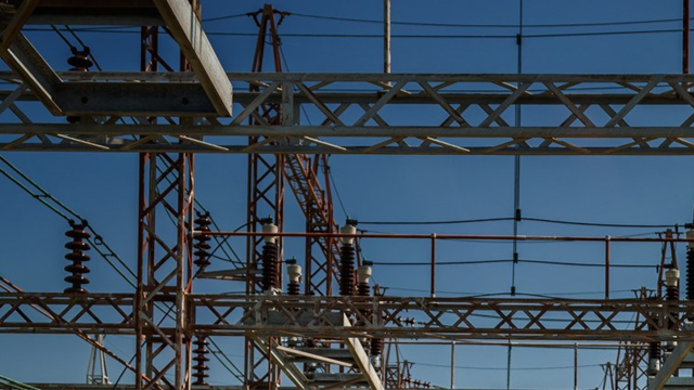 Struktur av høyspentlinjer og transformatorer i en elektrisk stasjon under en klar blå himmel.