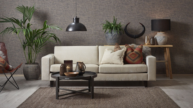 Stue med en lys sofa, dekorative puter, et svart bord, planter og stilige lamper på en teksturert vegg.