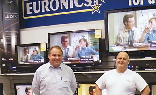 To menn står foran flere TV-er i en elektronikkbutikk, med Euronics-logoen synlig i bakgrunnen.