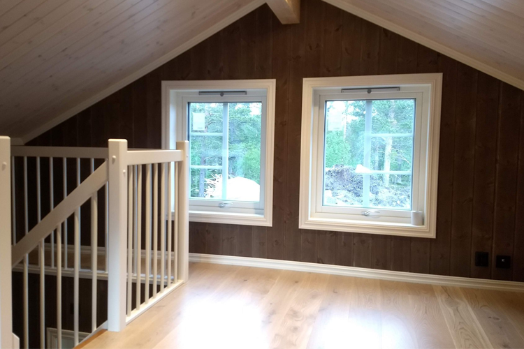 Lyst loft med trevegger, to vinduer og en hvit trapp som fører nedover.