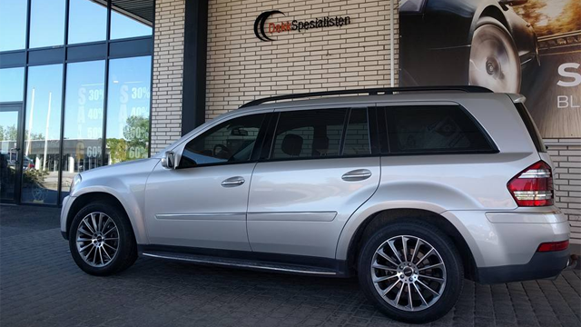 En sølvfarget SUV parkert foran en bilforhandler med moderne fasade.