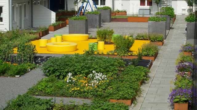 En fargerik hage med gule sitteplasser, grønne planter og blomster i forskjellige farger, omgitt av grå steinheller.