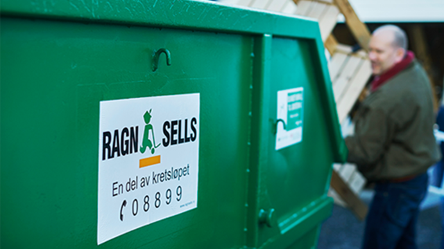 Grønn avfallscontainer med Ragna Sells-logo og kontaktinformasjon, med en person i bakgrunnen som bærer materialer.