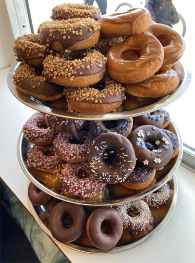 Tre etasjer med fargerike donuts, inkludert sjokoladeglasur, strøssel og nøtter, stablet på en sølvfat.