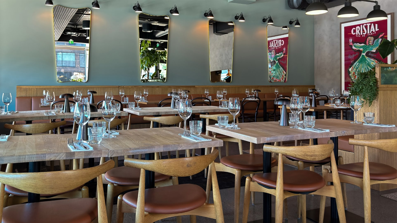 Moderne restaurant med tre bord, stoler og glass, samt speil og kunstverk på veggene.