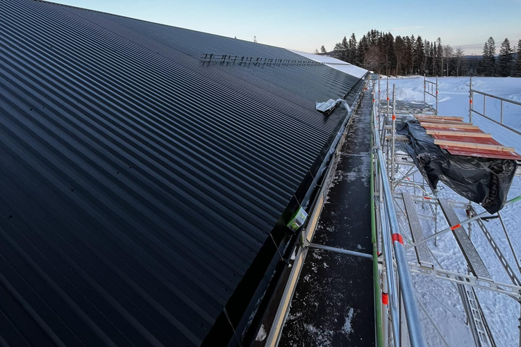 Takrenovering på et svart tak med snø og stillas i bakgrunnen.