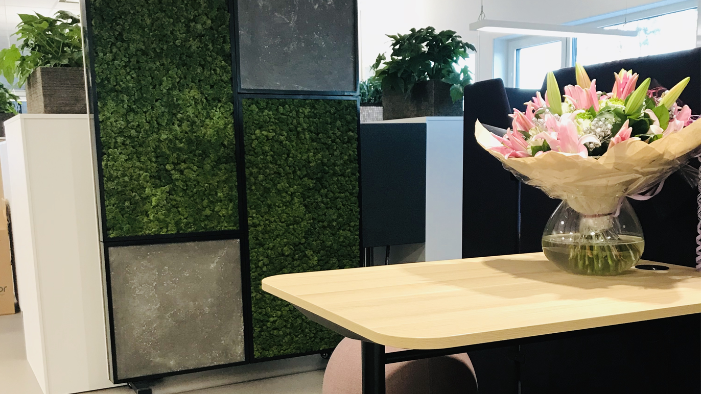 Moderne kontorinnredning med en blomsterbukett på et bord og grønne planter i bakgrunnen.