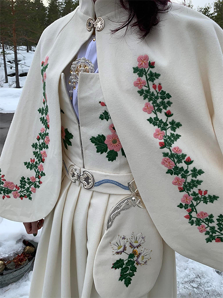 Kvinne iført tradisjonell bunad med blomsterbroderi, stående i snølandskap.
