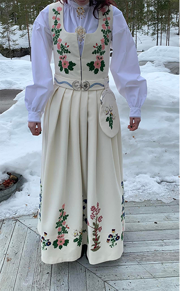 Kvinne iført en tradisjonell bunad med blomsterbroderi, stående på snøfylt bakgrunn.
