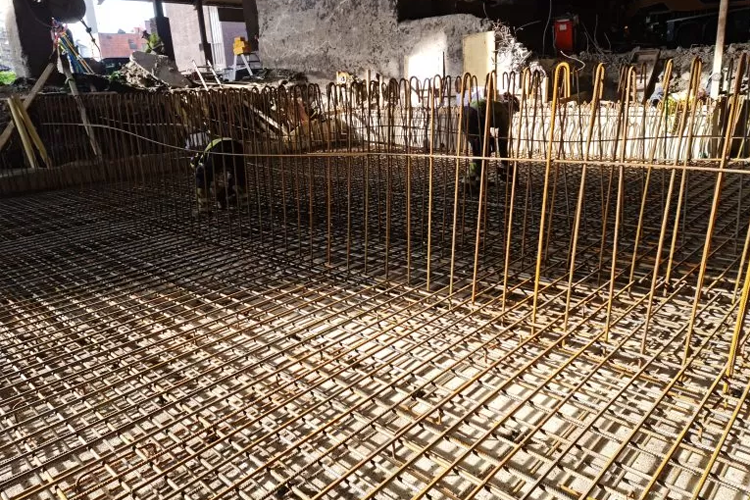 Bilde av armeringsjern på en byggeplass, klart for støping av betong. Sollys skinner på det metalliske nettet.