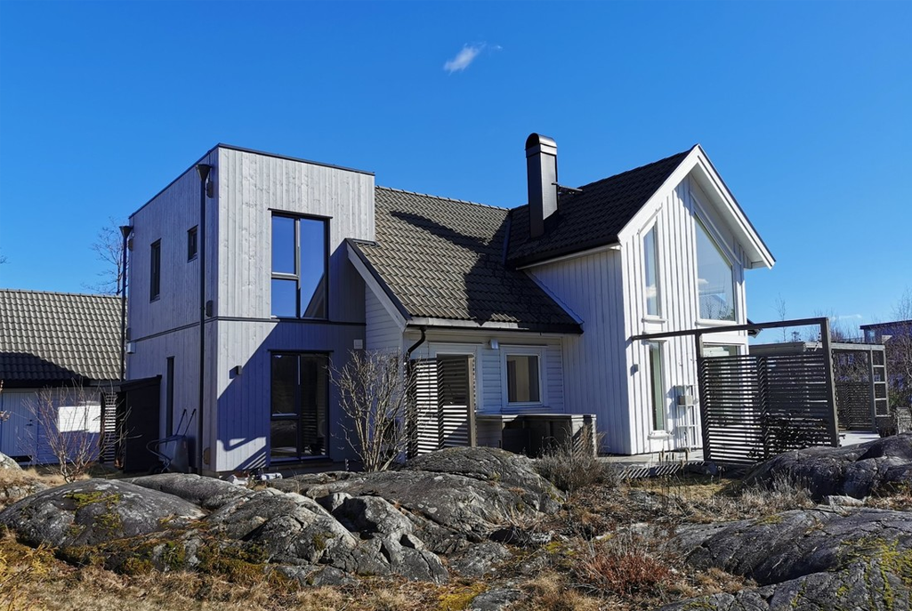 Moderne enebolig med trepanel og skråtak, beliggende på steinete grunn under blå himmel.