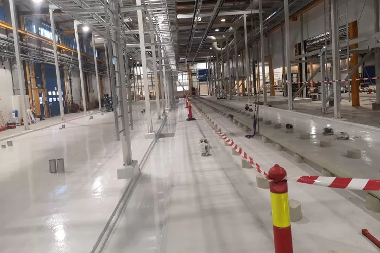 Bilde av en stor, tom industrihall med hvit gulv, stålstøtter og avsperringer i rød og hvit.