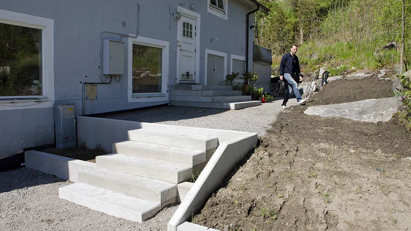 En mann går ned trappen til et hus med gruslagt gårdsplass og nyplantet hage.