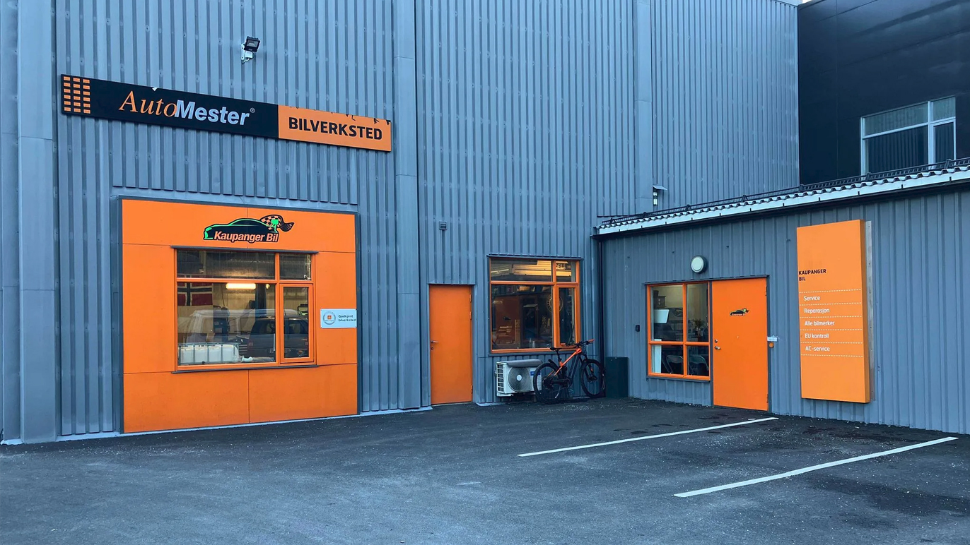 Bilde av Autolager med oransje detaljer og inngang til verkstedet, parkert sykkel foran.