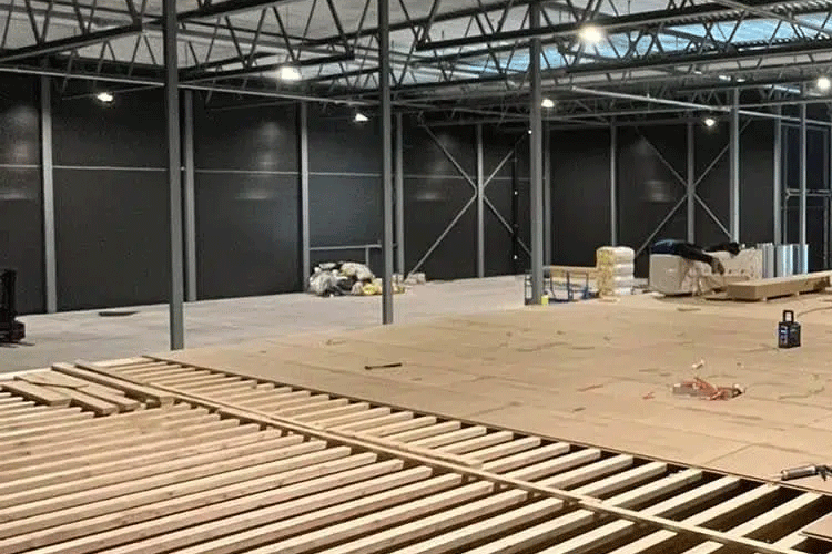 En stor, tom lagerbygning med treplanker på gulvet og svarte vegger i bakgrunnen.